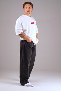 White cotton t-shirt with a red printed label, paired with loose-fitting black denim jeans and white sneakers. Plain background.