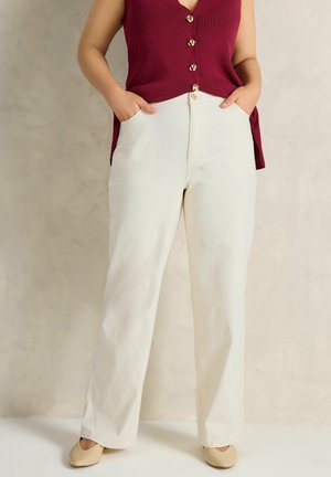Woman wearing off-white straight-leg pants with pockets, paired with a sleeveless burgundy buttoned top and beige flat shoes.