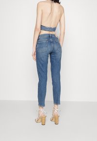 Vaqueros de mezclilla con un corte clásico, lavado medio y bolsillos traseros. Combinados con un top de mezclilla corto y sandalias de tacón beige.