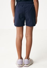 Pantalones cortos de algodón azul marino con cinturilla elástica, que presentan un diseño sencillo y corte recto. Combinados con zapatillas de deporte moradas claras.
