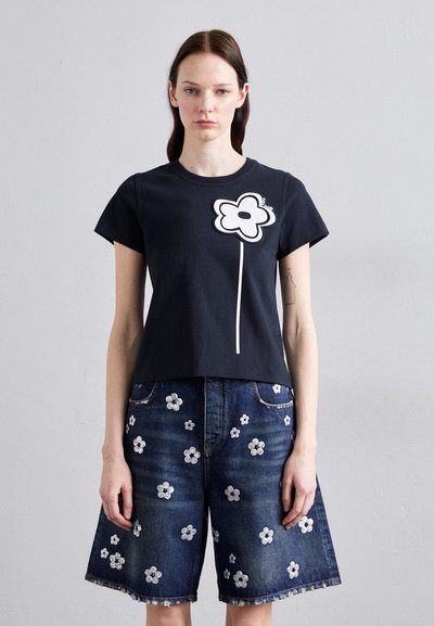 Μαύρο κοντομάνικο t-shirt με μεγάλο λευκό γραφικό άνθος στο μπροστινό μέρος, σε συνδυασμό με τζιν σορτς που έχουν διασκορπισμένη λευκή κεντητή ανθοδέσμη.