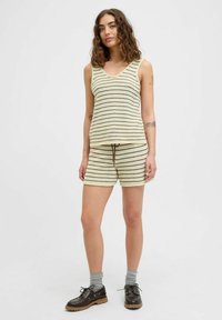 Randig ärmlös topp i kräm och brunt med V-hals; matchande shorts med dragsko. Materialet ser ut att vara texturerat; ihop med mörka skor.