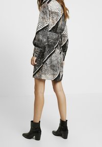 Long-sleeved dress with a black and white snake print pattern, featuring diagonal stripes and a relaxed fit. Pair with black ankle boots.