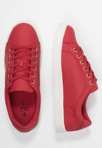 Baskets rouges avec une surface lisse texturée et des accents en maille, dotées de lacets ronds, d'œillets métalliques et d'une semelle en caoutchouc blanche.