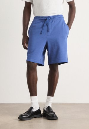 Blå bomullsblandade shorts med elastisk midja och snörning. Bärs med vita strumpor och svarta loafers, vilket visar en avslappnad passform.