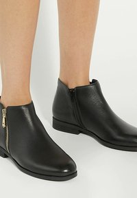 Bottes noires à la cheville en cuir lisse avec un bout pointu. Dotées d'une fermeture éclair sur le côté et d'un petit talon. Design simple et épuré, adapté à diverses tenues.