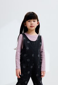 Salopette en denim noir à pois gris, associée à un t-shirt à manches longues violet clair. Comprend des poches avant et une coupe décontractée.