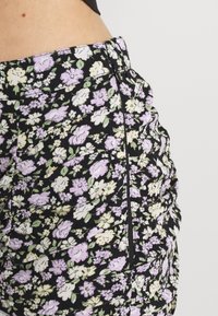 Květinová sukně s černým pozadím, zdobená světle fialovými a žlutými květy. Nařasený design, boční zip. Vyrobena z měkké látky.