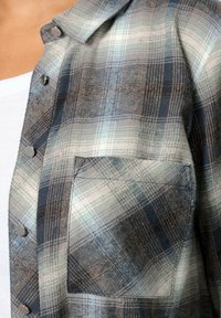 Rutigt skjorta i nyanser av blått och grått, med knäppning fram, bröstficka och ett något strukturerat tyg.