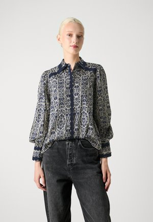 Navy og cremet mønstret bluse med krave, knapfront og puffede lange ærmer. Sammen med højtaljede sorte jeans.