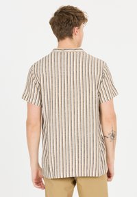 Kortärmad randig skjorta i beige och marinblått. Har vertikala ränder, en avslappnad krage och en rak nederkant. Mjuk textur.