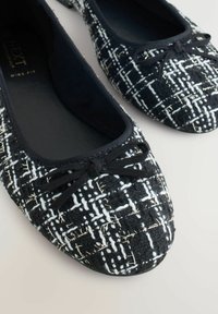 Balerini texturate în alb și negru cu un aspect împletit, având o fundă din panglică neagră pe vârf și un interior cu pernuță.