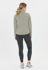 Ljusgrå jacka med en strukturerad baksida, kombinerad med svarta leggings och silverfärgade sportskor. Reflexdetaljer på leggings.