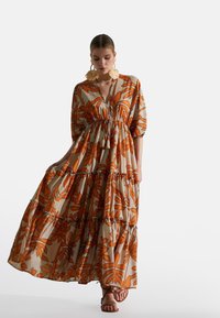 Maxikleid aus leichtem Stoff mit Orangeblattmuster auf beigem Hintergrund, verfügt über einen V-Ausschnitt, schichtweise Gestaltung und Puffärmel.