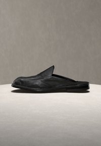 Mule παπούτσι από μαύρο δέρμα, χωρίς κορδόνια, με χαμηλό τακούνι, εκτεθειμένο σε ουδέτερη επιφάνεια πάνω σε απλό φόντο.