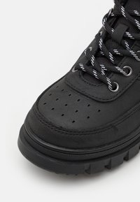 Czarne sneakersy z gładkim wierzchem z perforacjami, czarno-białymi sznurówkami w paski oraz teksturowaną podeszwą z rowkami zapewniającymi przyczepność.