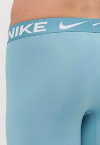 Lyseblå atletiske leggins med en glat tekstur og et hvidt "NIKE" logo på det elastiske taljebånd. Har et tætsiddende design og sømløs konstruktion.