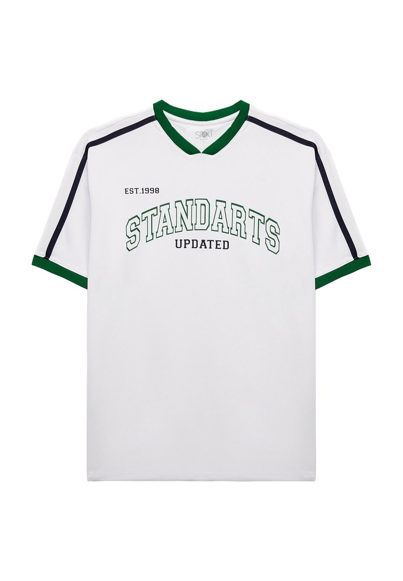 Camiseta blanca con acentos verdes y negros, con cuello en V y el texto "STANDARTS UPDATED" en el pecho junto con "EST.1998."