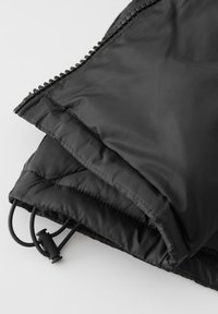 Zwarte pufferjack met een gladde, glanzende buitenkant en gewatteerde textuur. Voorzien van een rits en verstelbare koorden aan de zoom voor een goede pasvorm.