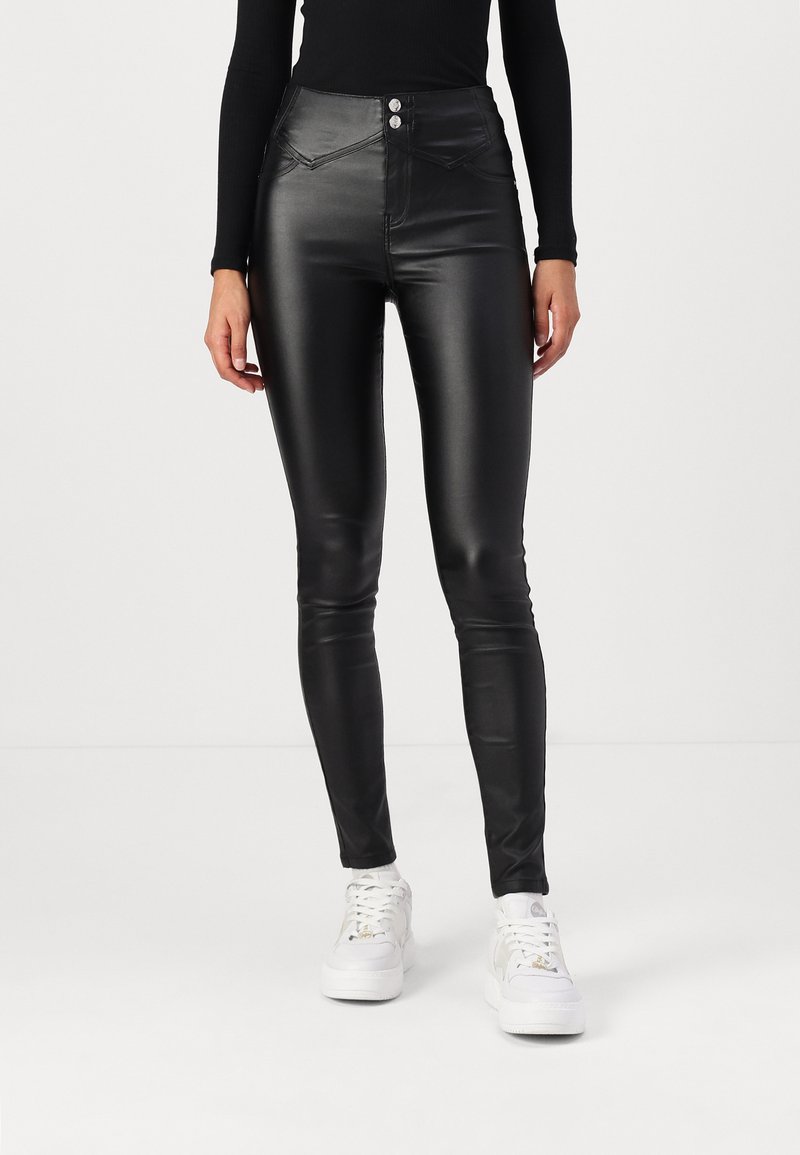 Zwarte, high-waisted nepleren broeken met twee voorzakken en zichtbare stikdetails. Strak ontwerp, gecombineerd met witte sneakers.