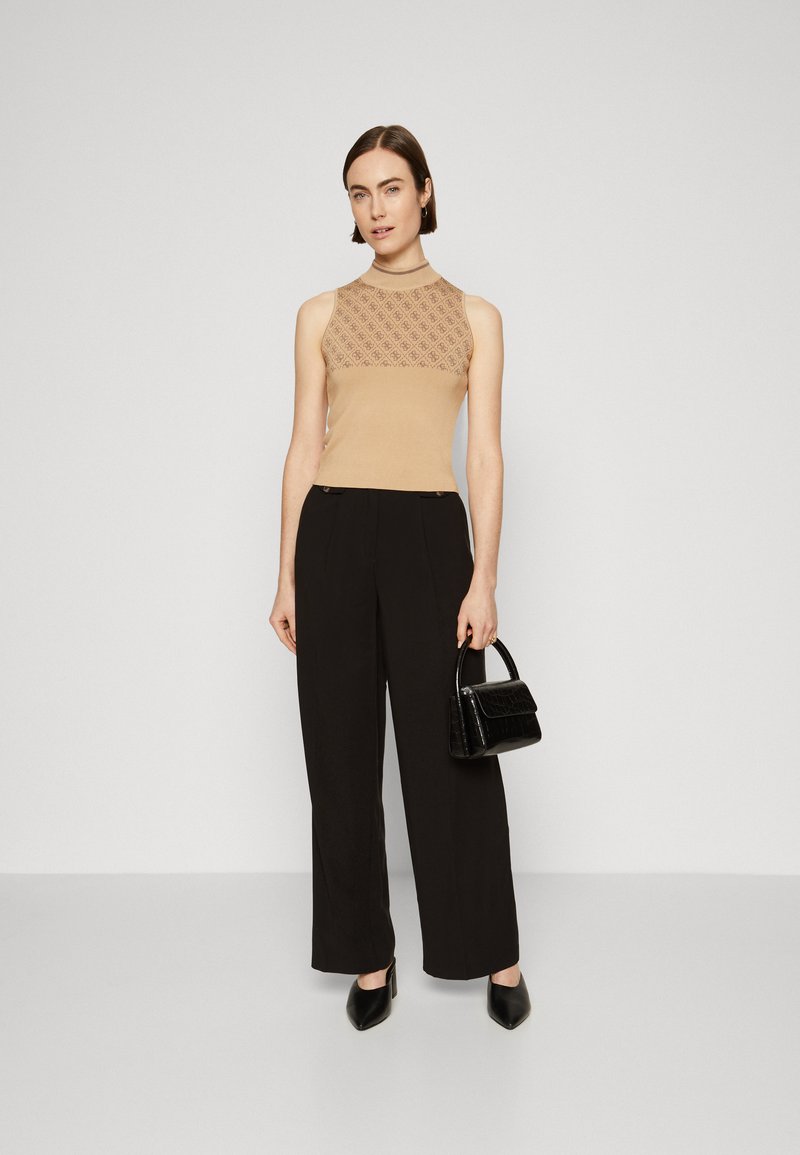 Top beige senza maniche con design a fantasia, pantaloni neri a gamba larga e una piccola borsa nera con texture. Le scarpe sono nere, a punta e con tacco basso.