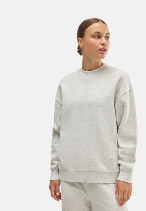 Sudadera gris con cuello redondo, hombros caídos y puños acanalados. Logo bordado sutil en la parte inferior izquierda delantera.