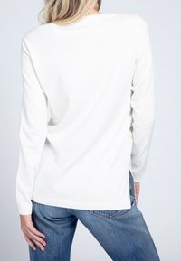 Maglione bianco a maniche lunghe realizzato in tessuto morbido, con scollo rotondo e spacchi laterali, abbinato a jeans blu.