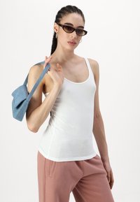 Top de tirantes blanco ajustado hecho de una tela suave, combinado con pantalones de chándal rosas y un pequeño bolso de mezclilla. El modelo lleva gafas de sol oscuras.