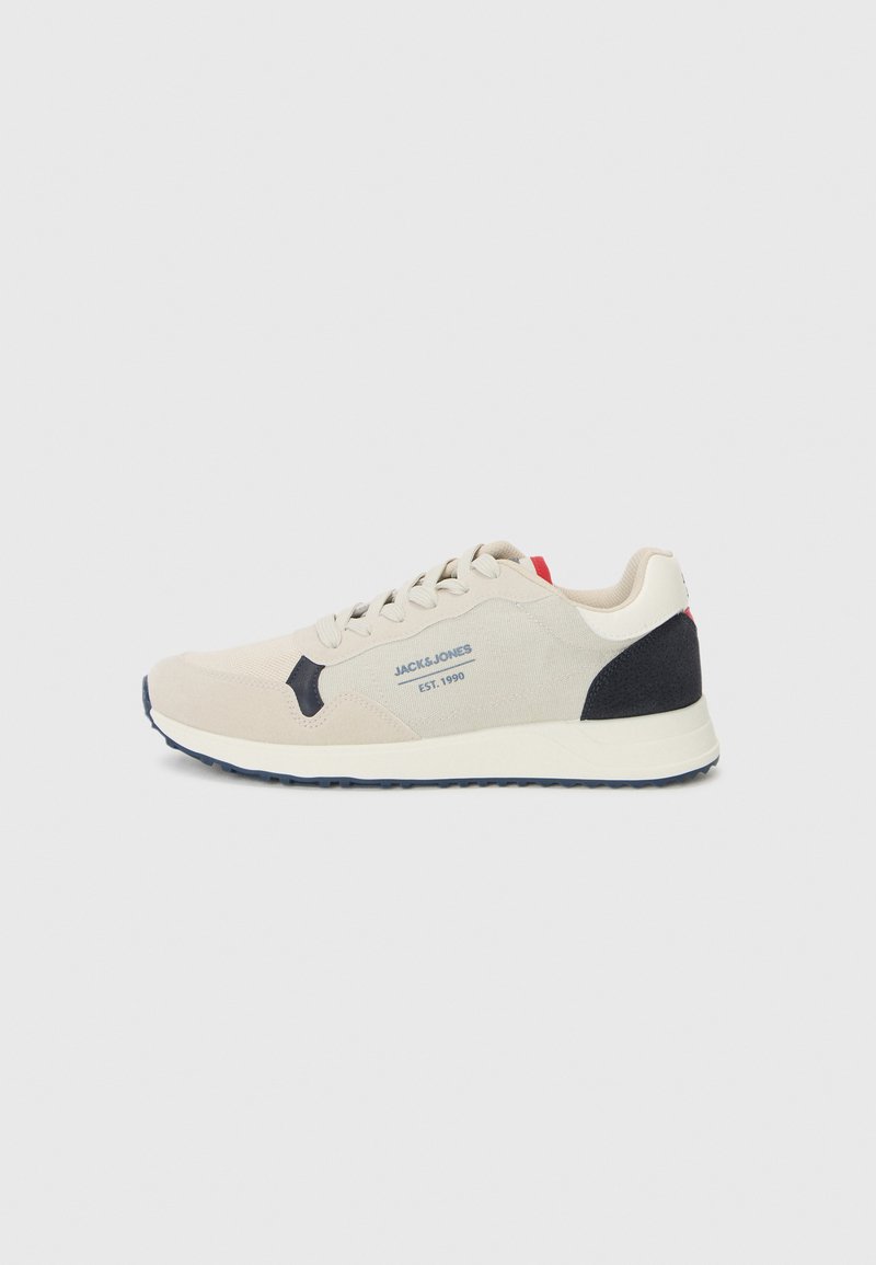 Beige athletic shoe with a suede and textile upper, dark blue accents on the heel and outsole, and lace-up front with logo detail.