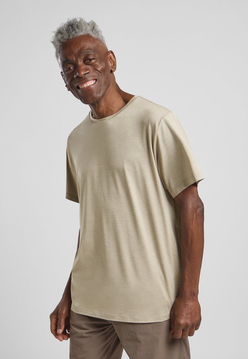 Hellbeige, kurzärmliges T-Shirt mit runder Halsausschnitt, glatter Textur und lockerer Passform. Tragen von einer lächelnden Person.