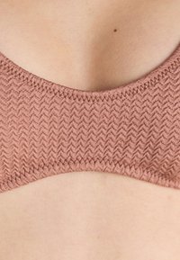 Hnedý textúrovaný bralet s cik-cak vzorom, má zaoblený výstrih a bezšvové okraje pre pohodlie. Mäkkučký materiál s miernym elastickým efektom.