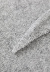 Tela de punto gris con una textura suave y difusa. Presenta un dobladillo puntiagudo y variaciones sutiles en el tono que le aportan profundidad.