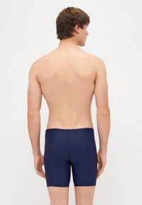 Σκούρο μπλε μαγιό από ομαλό, ελαστικό ύφασμα. Διαθέτει απλό σχέδιο με ελαστική μέση και μήκος μέχρι το μέσο του μηρού.