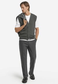 Grå ribbad stickad väst över en vit t-shirt, kombinerad med mörkgrå skräddarsydda byxor och svarta loafers. Enkel och nutida design.