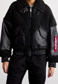 Schwarze Bomberjacke aus einer Mischung von Lammfell und Leder, mit durchgehendem Reißverschluss, gerippten Bündchen und dem Tag "REMOVE BEFORE FLIGHT".
