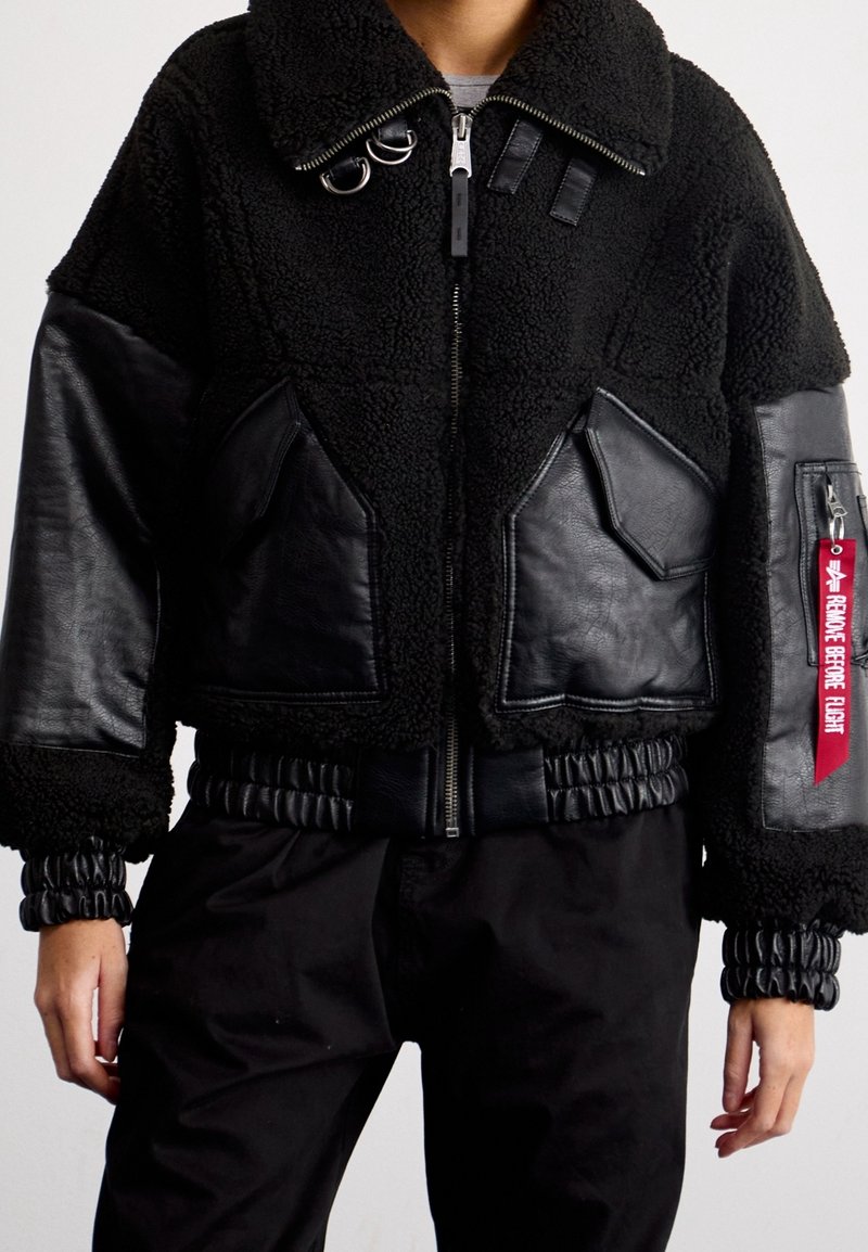 Schwarze Bomberjacke aus einer Mischung von Lammfell und Leder, mit durchgehendem Reißverschluss, gerippten Bündchen und dem Tag "REMOVE BEFORE FLIGHT".