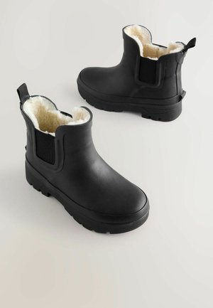 Fekete, gumiból készült bokacipők, texturált felülettel, plüss krémszínű béléssel, rugalmas oldalsó panelekkel és húzófüllel a könnyű felhúzás érdekében.