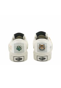 Baskets blanches en tissu texturé, avec des motifs de pattes vertes et de tigres sur les patchs au niveau des talons, semelles en caoutchouc et doublure intérieure noire.