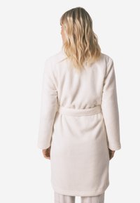 Biały, pluszowy szlafrok z długimi rękawami, przewiązywany w talii, o miękkiej teksturze. Widok z tyłu ukazuje gładki materiał i minimalistyczny design.