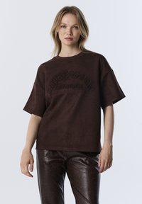 T-shirt court marron à manches courtes en tissu doux, avec un texte en relief "IMPRESSION SELF BELIEVE" sur le devant ; coupe décontractée.