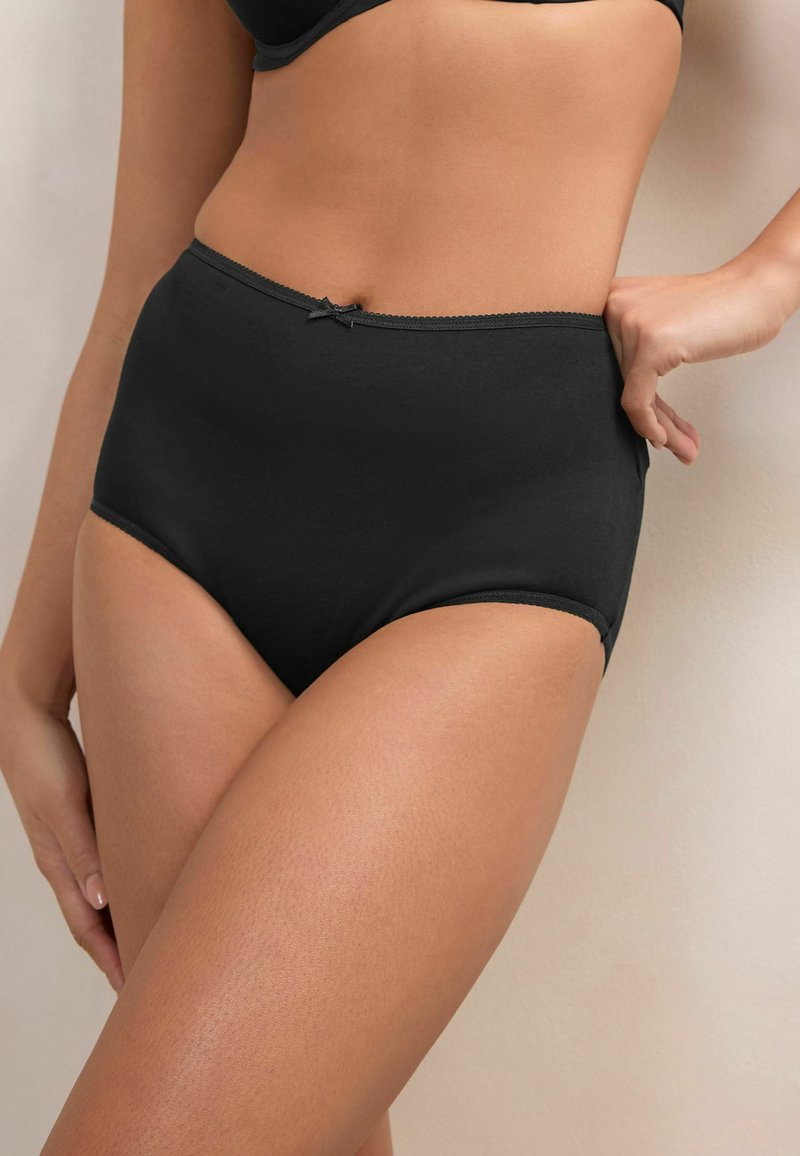 Hochgeschnittene schwarze Baumwollunterwäsche mit glatter Textur und gewelltem Saum, versehen mit einer kleinen Schleifenakzent auf dem Bund.