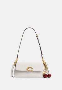 Sac à épaule en cuir blanc avec fermoir doré et bandoulière noire, orné d'un porte-clés cerise doré et rouge.