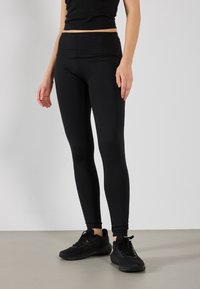 Svart leggings laget av elastisk materiale, med høy midje og en tettsittende design. Kombinert med svarte joggesko.