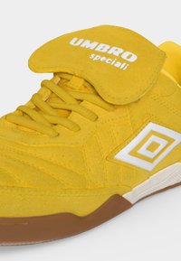 Κίτρινο suede αθλητικό παπούτσι Umbro Speciali με λευκό λογότυπο, ασφαλισμένα κορδόνια και αναδιπλούμενη γλωττίδα, με καφέ λαστιχένια σόλα.
