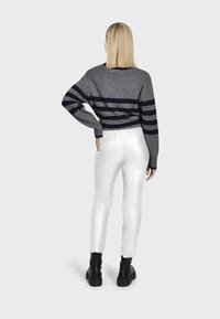 Grijze trui met marineblauwe strepen, gecombineerd met glanzende witte broek. Zwarte enkellaarsjes. Uitzicht van achter, met details van schouders en taille.
