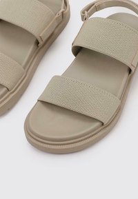 Sandalias beige con dos amplias correas de textil, un acabado texturizado y una suela de goma moldeada con un ligero borde para mayor agarre.