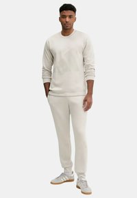 Felpa leggera beige e pantaloni della tuta aderenti abbinati, realizzati in tessuto morbido, con polsini a costine e collo rotondo.