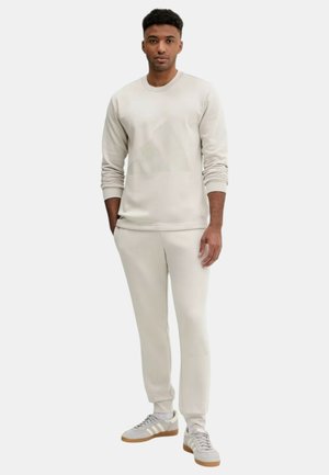 Felpa leggera beige e pantaloni della tuta aderenti abbinati, realizzati in tessuto morbido, con polsini a costine e collo rotondo.