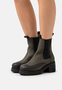 Green leather ankle boots feature elastic side panels, a rounded toe, and a textured black sole with a chunky heel.