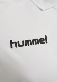 Hvid polo skjorte med et sort "hummel" logo på brystet, lavet af et glat, åndbart stof; har et klassisk kravedesign.